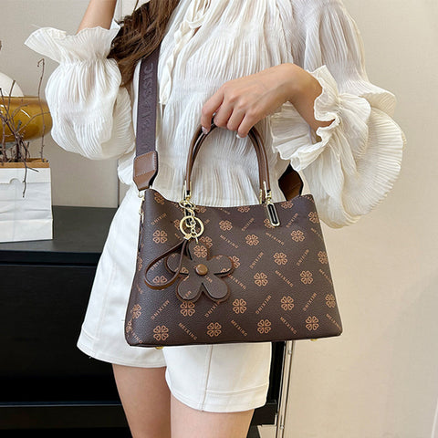 CJ brown floral pendant crossbody bag with flower charm and adjustable strap held by woman in white blouse